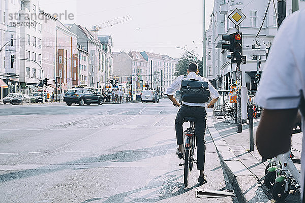 Rückansicht eines Geschäftsmannes mit Fahrrad  der am Straßenverkehrssignal in der Stadt steht
