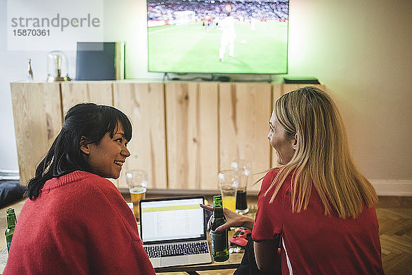 Lächelnde Freundinnen unterhalten sich während des Fußballspiels zu Hause