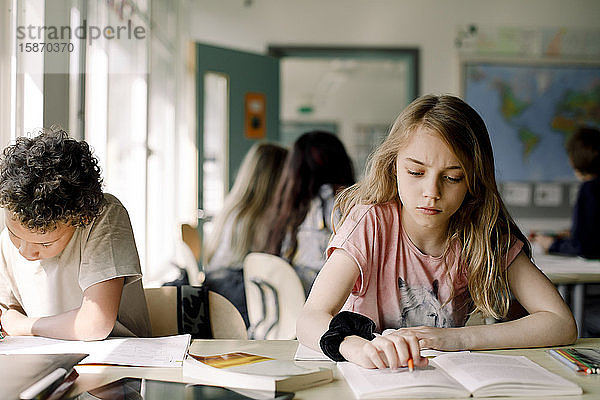 Weibliche Studentin lernt aus einem Buch  während sie im Klassenzimmer neben einem männlichen Freund sitzt