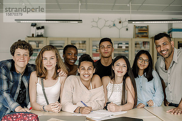 Porträt eines lächelnden Professors mit jugendlichen Studenten am Tisch im Klassenzimmer