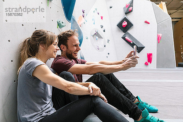 Glücklicher Mann  der mit einer Freundin im Fitnessstudio per Smartphone Selbsthilfe betreibt