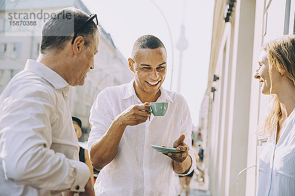 Lächelnder Geschäftsmann trinkt Kaffee mit Kollegen im Straßencafé in der Stadt