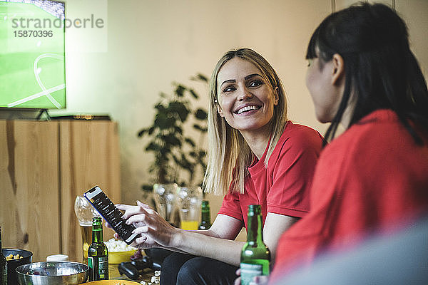 Lächelnde Frau mit Smartphone  die einen Freund anschaut  während sie zu Hause Fußball schaut