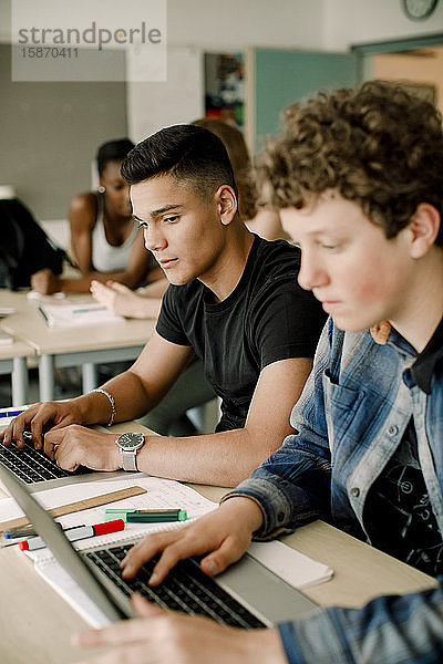 Männliche Studenten benutzen Laptop  während sie im Klassenzimmer am Tisch sitzen