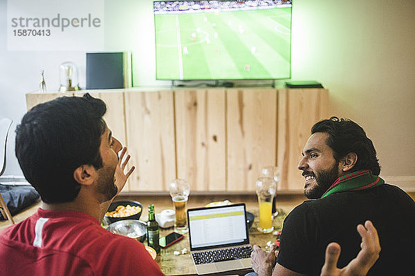 Männliche Freunde unterhalten sich beim Fußballschauen im Wohnzimmer