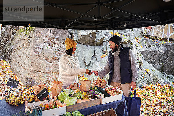 Lächelnde Frau hält Kreditkartenlesegerät für männlichen Kunden am Marktstand