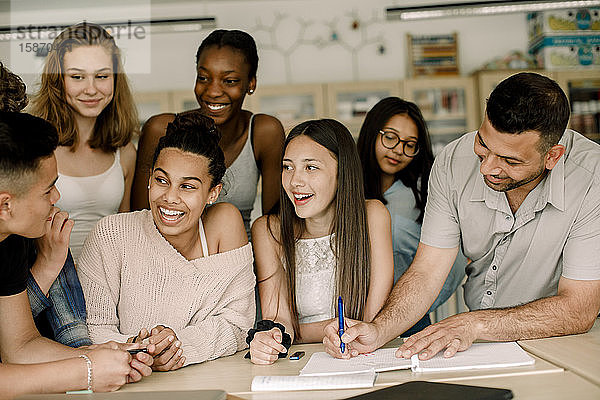 Lächelnde Schüler schauen einen Teenager an  während der Lehrer im Klassenzimmer über dem Tisch unterrichtet