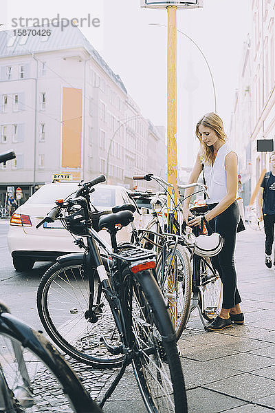 Jungunternehmer schließt Fahrrad in voller Länge auf dem Bürgersteig in der Stadt ein