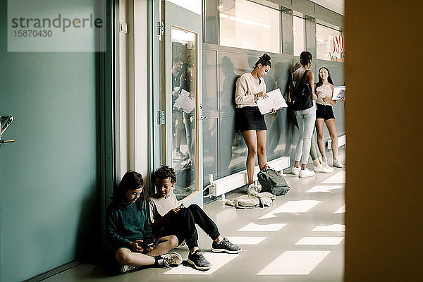 Junge und Mädchen sitzen in der Tür  während sich Schüler der Mittelstufe auf dem Schulkorridor unterhalten