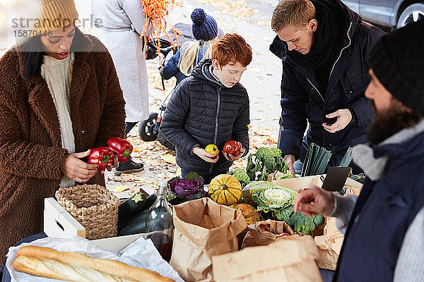 Familie kauft frische Paprikaglocken von männlichem Verkäufer am Marktstand