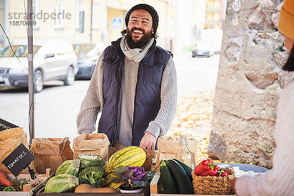 Lächelnder Mann kauft am Obststand frisches Gemüse von einer Marktverkäuferin