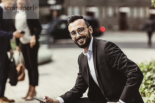 Porträt eines lächelnden Geschäftsmannes mit Mobiltelefon  der im Freien sitzt