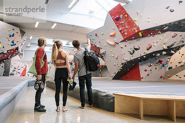 Rückansicht eines Mannes  der auf die Wand zeigt  während er bei der Frau und dem Trainer in der Turnhalle steht