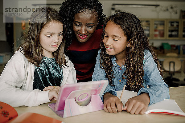 Tutorin mit Schülerinnen  die sich im Klassenzimmer ein digitales Tablet ansehen