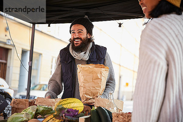 Lächelnder Mann kauft Gemüse von weiblichem Verkäufer am Marktstand