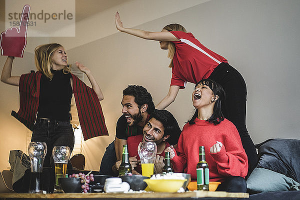 Glückliche männliche und weibliche Fans feiern  während sie zu Hause ein Fußballspiel sehen