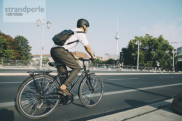 Geschäftsmann mit Helm fährt Fahrrad auf Straße in Stadt gegen Himmel
