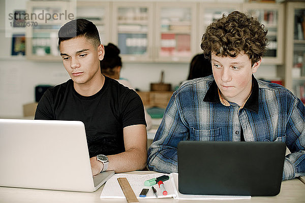 Männliche Studenten benutzen den Laptop über dem Tisch  während sie im Klassenzimmer sitzen