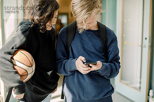 Männliche Schüler mit Smartphone auf dem Schulflur