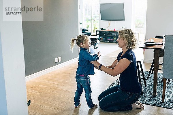 Seitenansicht der Mutter beim Ankleiden der Tochter  während sie zu Hause auf dem Boden kniet