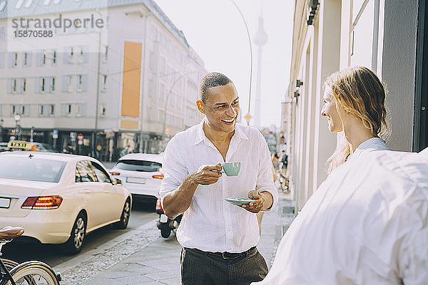 Lächelnder Geschäftsmann trinkt Kaffee mit einer Mitarbeiterin in einem Straßencafé in der Stadt