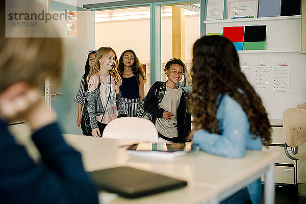 Lächelnde männliche und weibliche Schüler beim Betreten des Klassenzimmers
