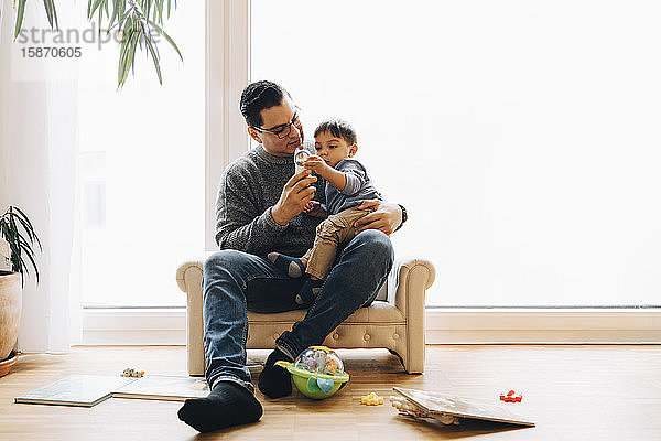 Vater spielt in voller Länge mit Kleinkind Sohn  während er zu Hause auf dem Sofa sitzt