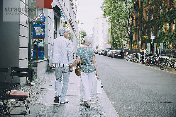 Ehepaar im Ruhestand hält sich beim Gehen auf dem Bürgersteig in der Stadt in voller Länge an den Händen