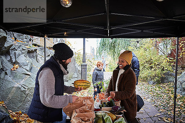 Lächelnde Frau kauft am Gemüsestand frischen Kürbis von männlichem Marktverkäufer