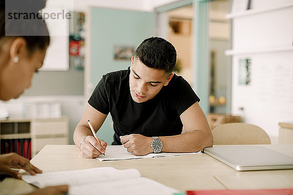 Männlicher Teenager schreibt  während er im Klassenzimmer sitzt