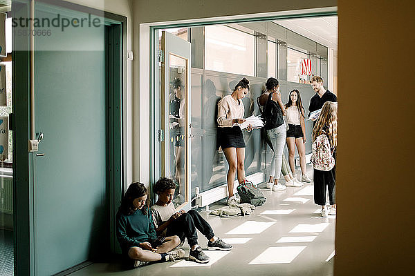Mädchen und Junge sitzen in der Tür  während der Professor im Schulflur mit den Studenten spricht