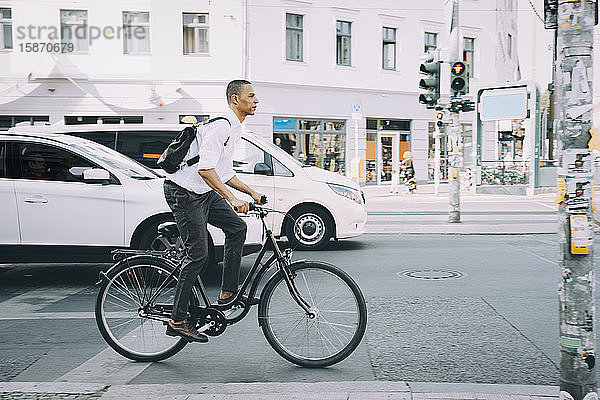 Fahrrad fahrender Geschäftsmann in voller Länge auf Bürgersteig gegen Gebäude in der Stadt