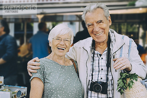 Porträt eines lächelnden älteren Paares mit Arm um den Arm auf dem Markt in der Stadt stehend
