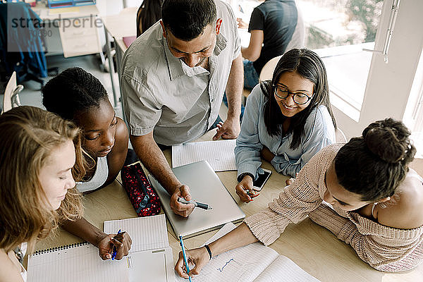 Schrägansicht von Teenagern  die studieren  während der Professor im Klassenzimmer am Tisch steht