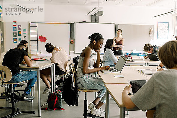 Schüler der Junior High studieren  während eine Lehrerin im Klassenzimmer steht