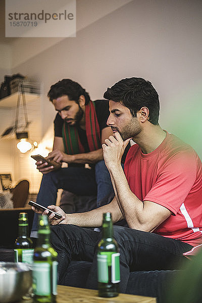 Männliche Fußballfans telefonieren mit dem Handy  während sie das Spiel zu Hause verfolgen