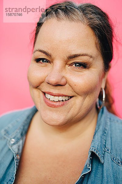 Porträt einer lächelnden reifen Frau vor rosa Hintergrund