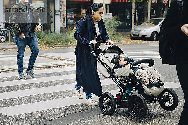 Mutter und Sohn sitzen in voller Länge im Kinderwagen und überqueren die Straße in der Stadt