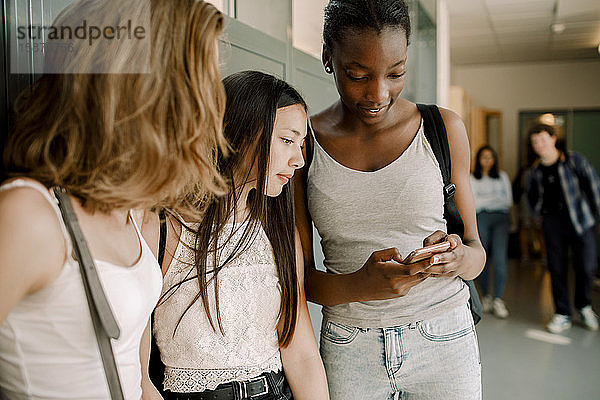 Schüler der Junior High School benutzen ein Smartphone  während sie im Schulkorridor stehen