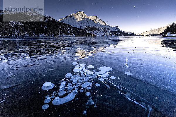 Methanblasen in der eisigen Oberfläche des Sees mit schneebedeckter Spitze  beleuchtet vom Mondlicht  Sils  Engadin  Graubünden  Schweizer Alpen  Schweiz  Europa