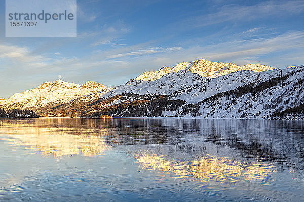 Von der Sonne beleuchtete Berge bei Sonnenuntergang  die sich auf der eisigen Oberfläche des Silsersees spiegeln  Engadin  Graubünden  Schweiz  Europa