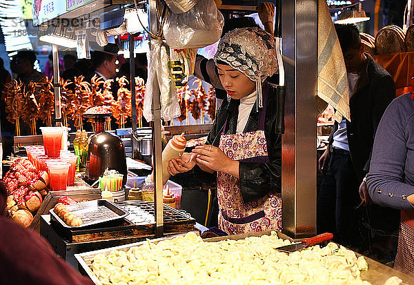 Muslimische Frau verkauft Lebensmittel an einem Stand auf dem Huajue-Nachtmarkt  Xian  Shaanxi  China  Asien