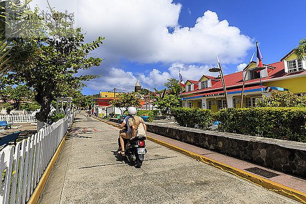 Paar auf Moped  bunte Stadt Bourg des Saintes  Terre de Haut  Iles Des Saintes  Les Saintes  Guadeloupe  Inseln unter dem Winde  Westindien  Karibik  Mittelamerika