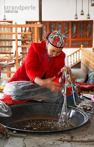 Uigurische Frau spinnt Seidenfaden aus Kokons in einer traditionellen Seidenwerkstatt  Jiya  Xinjiang  China  Asien
