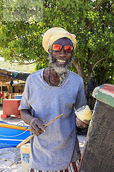 Grinsender Mann repariert Boot  farbenfrohe Saltwhistle Bay  Mayreau  Grenadinen  St. Vincent und die Grenadinen  Inseln über dem Winde  Westindische Inseln  Karibik  Mittelamerika