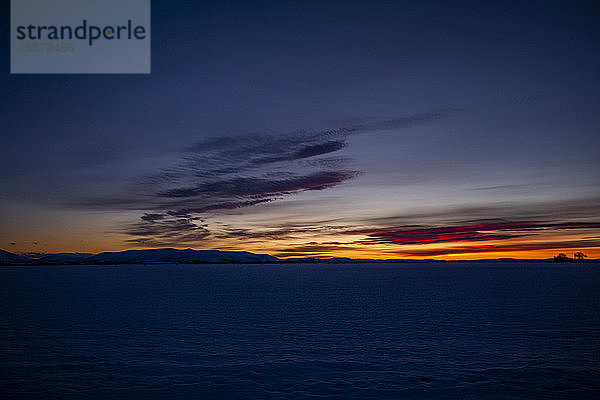 Verschneites Feld unter dramatischem Himmel bei Sonnenuntergang