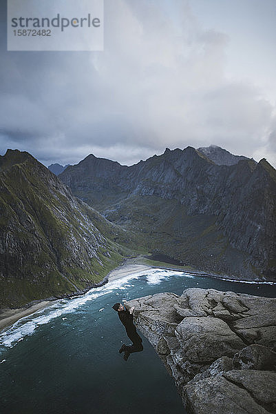 Mann hängt an einer Klippe am Berg Ryten auf den Lofoten  Norwegen