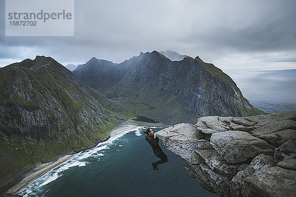 Mann hängt an einer Klippe auf dem Berg Ryten auf den Lofoten  Norwegen