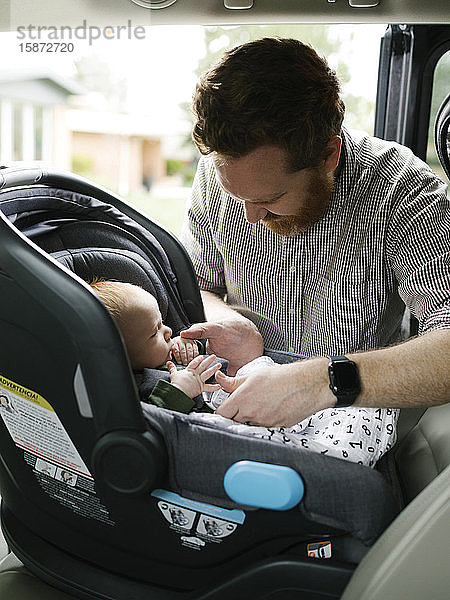 Vater schnallt kleinen Jungen (2-3 Monate) im Autositz an