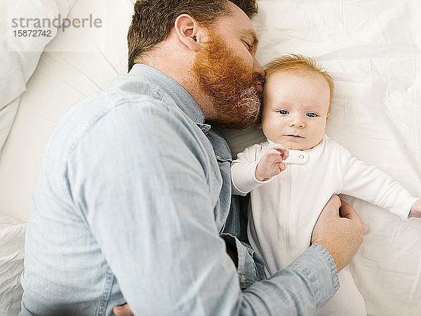 Vater küsst kleinen Jungen (2-3 Monate)  während er auf dem Bett liegt